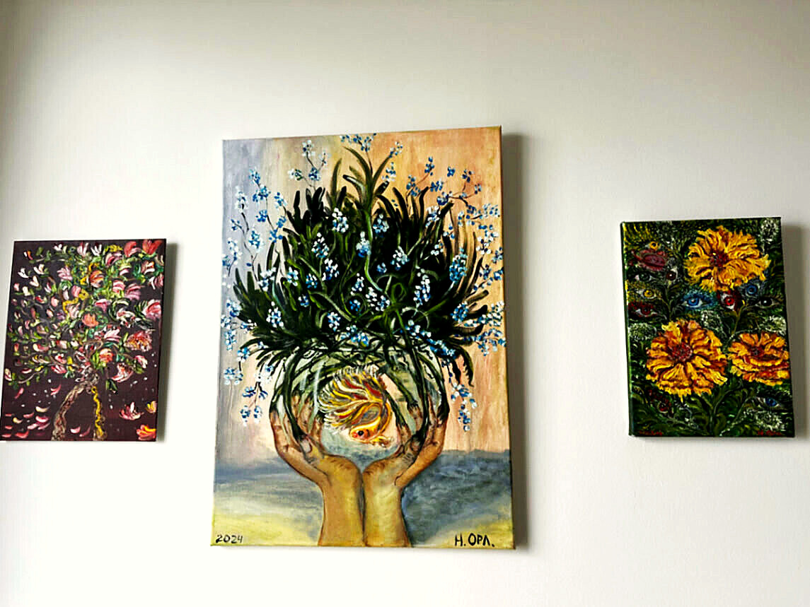 Three painted canvases on a white wall, with Nata Orlo’s fish painting in the centre