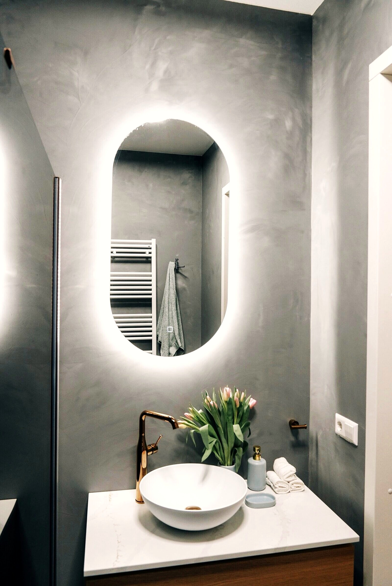 Bathroom with a back-lit oval mirror, vessel basin and brass fittings