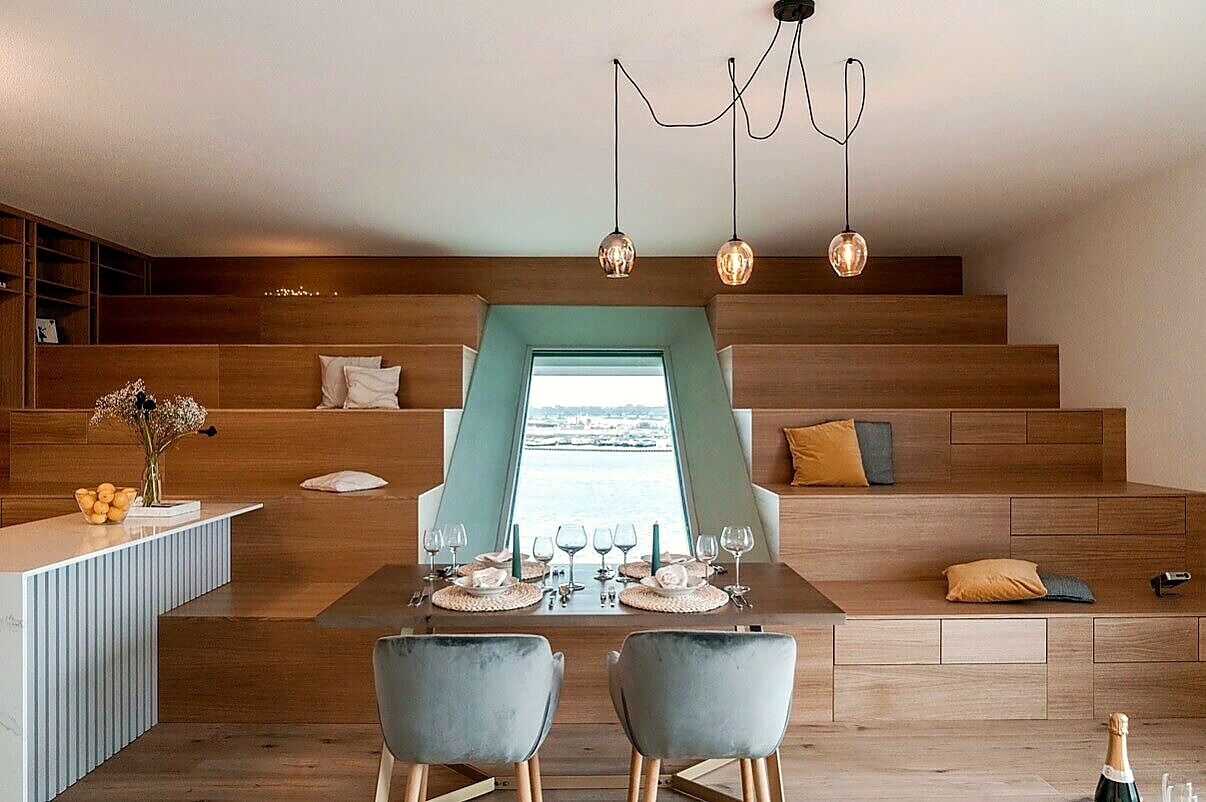 Dining table set for four in front of a stepped timber seating nook and a window over the water