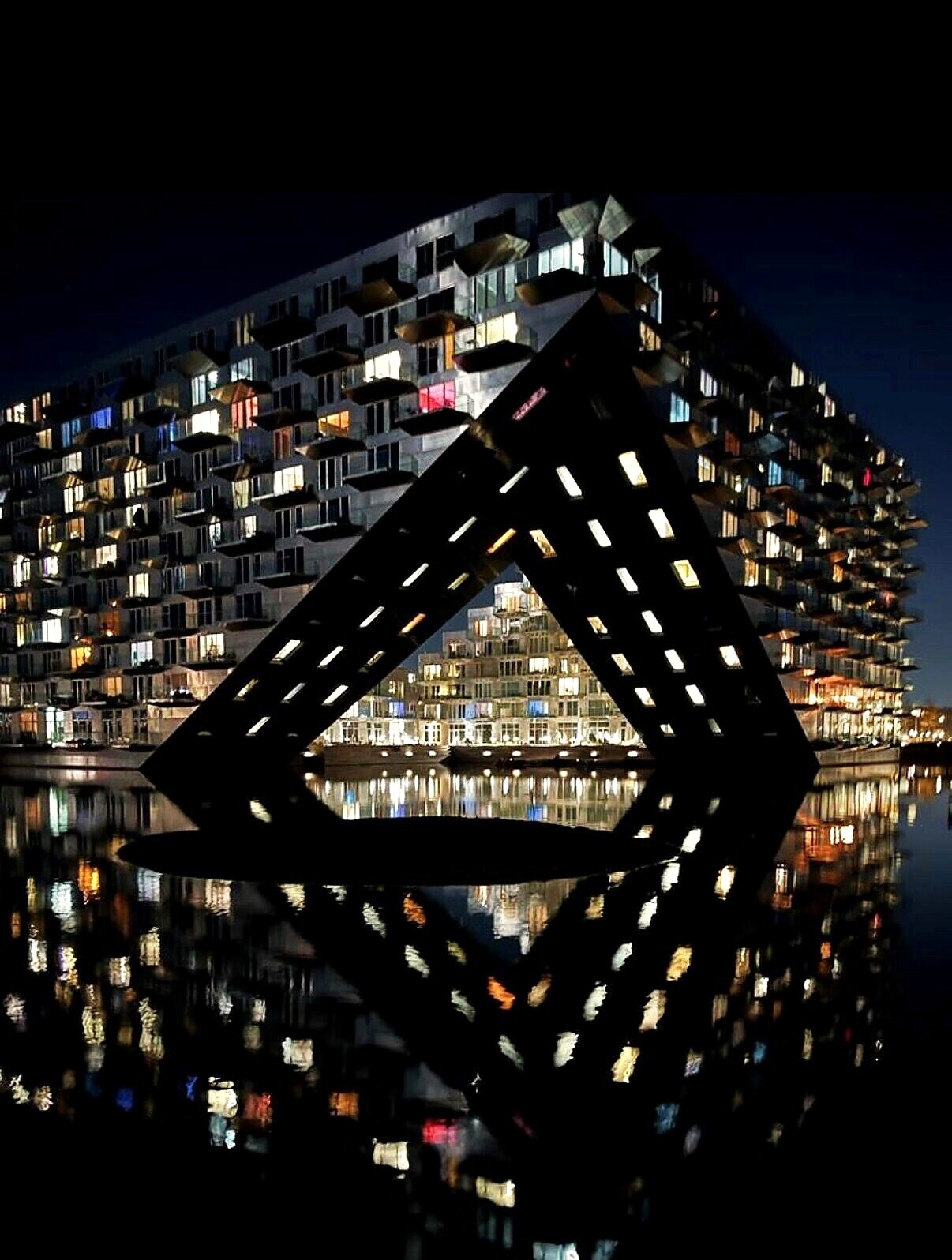 Lit windows and the arch reflected in black water at night
