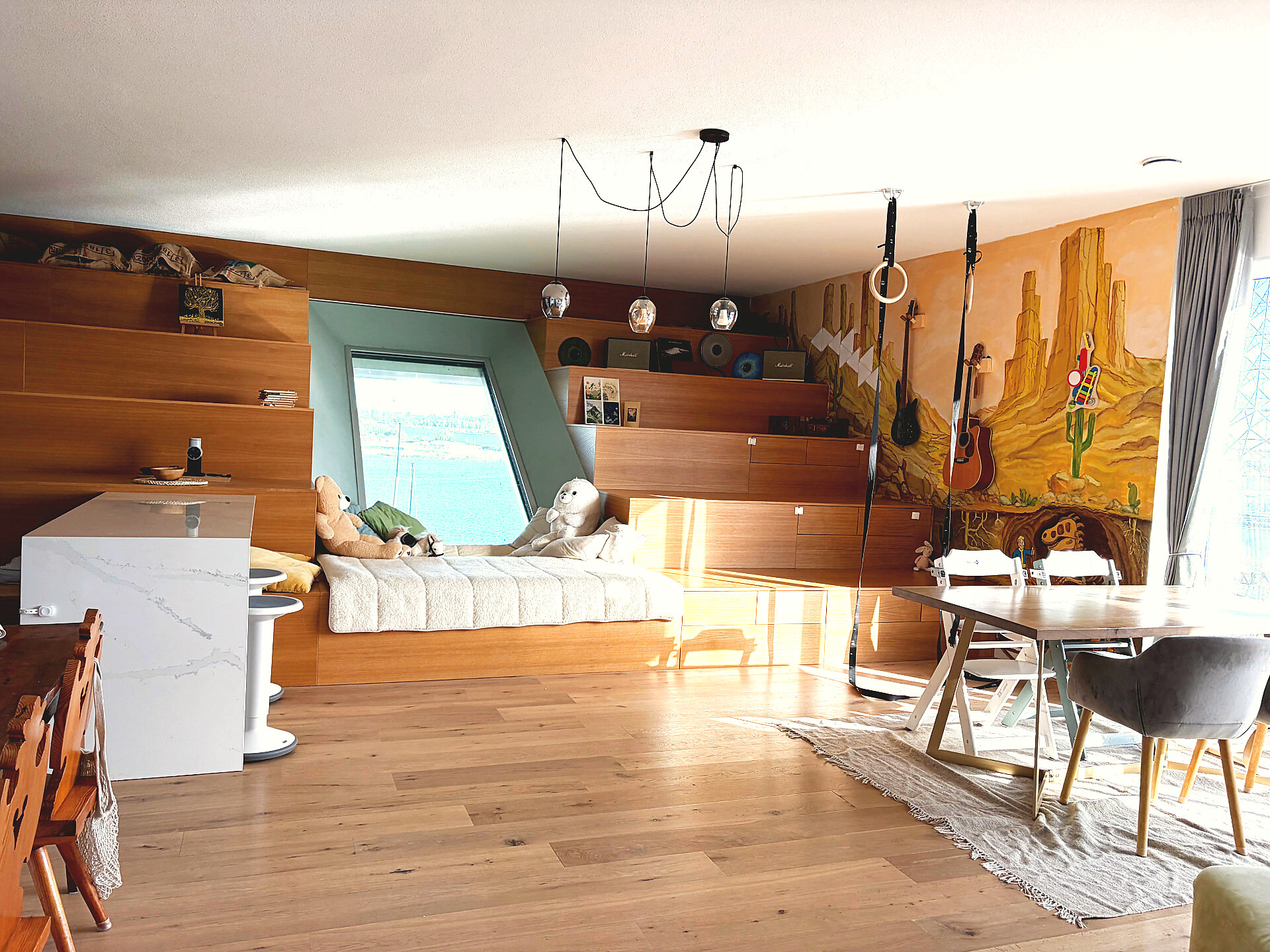Sunny open living room with built-in daybed, mural, dining table and a view over the water