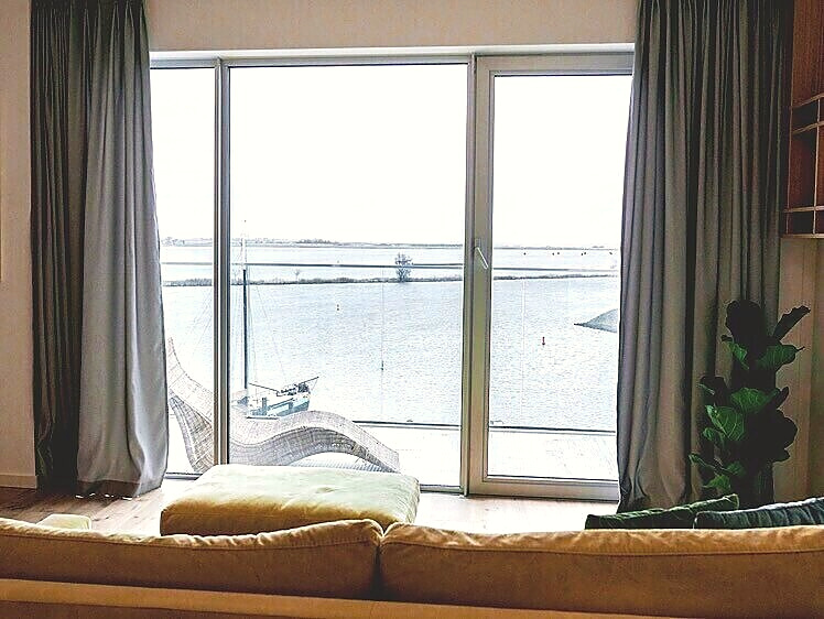 View from the sofa through full-height windows over the calm water — Nature’s TV