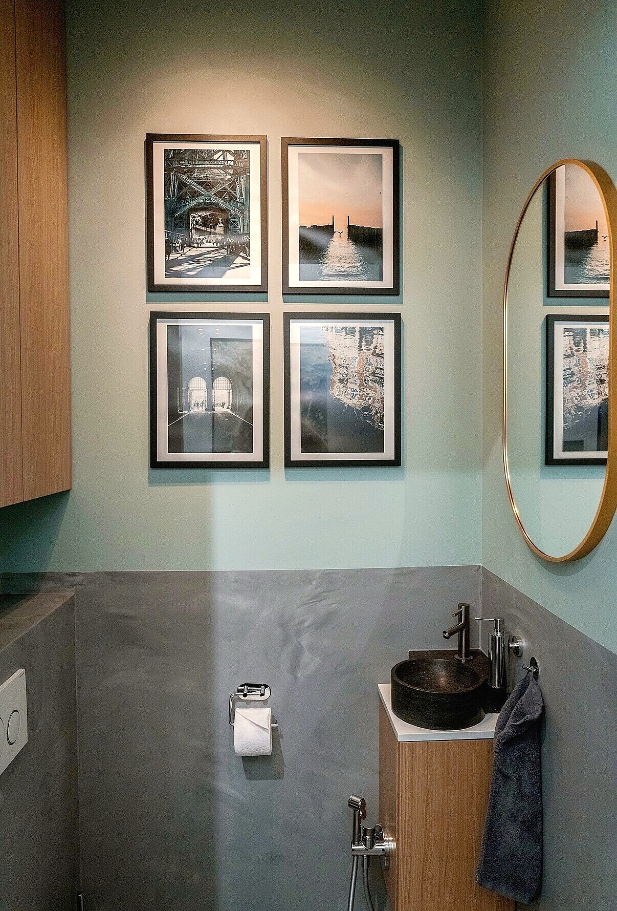 Toilet with four framed photos on the wall and an oval mirror