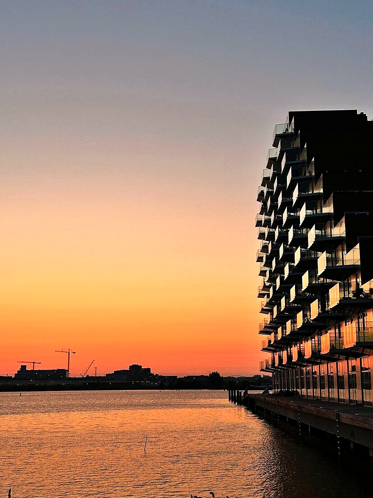 The boardwalk along the water at the foot of the building, against an orange sunset